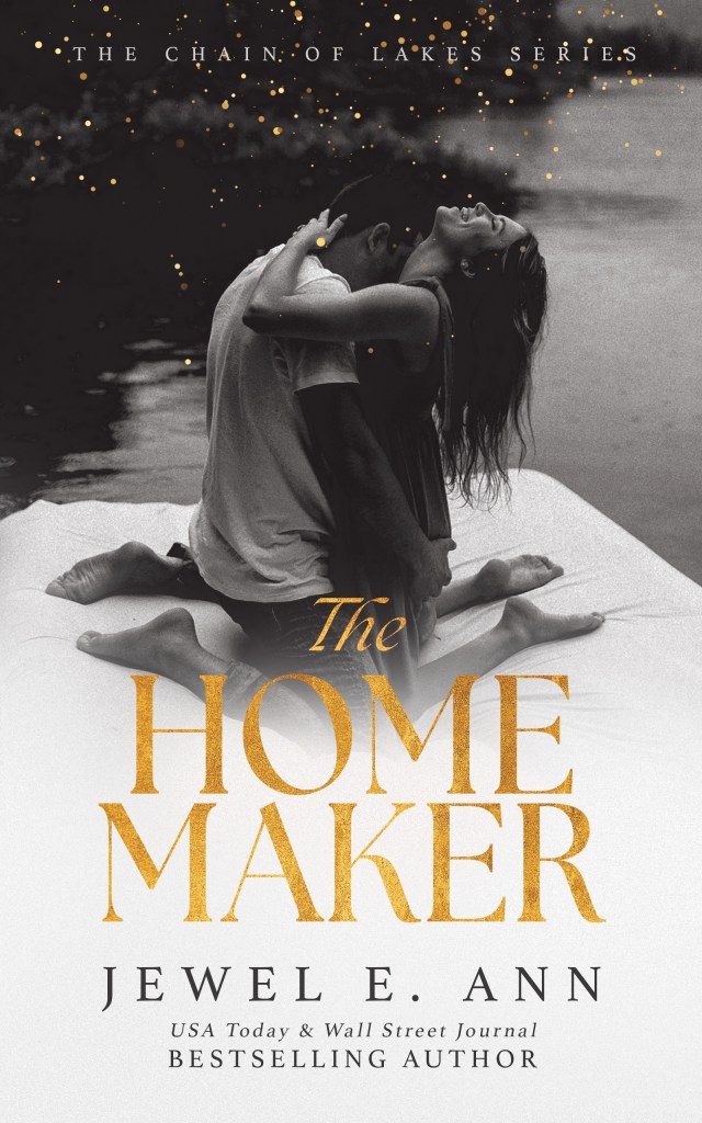 Cover image of 'The Homemaker' by Jewel E. Ann, featuring a romantic scene with a couple embracing by a lake. The title and author's name are prominently displayed in gold and white lettering.